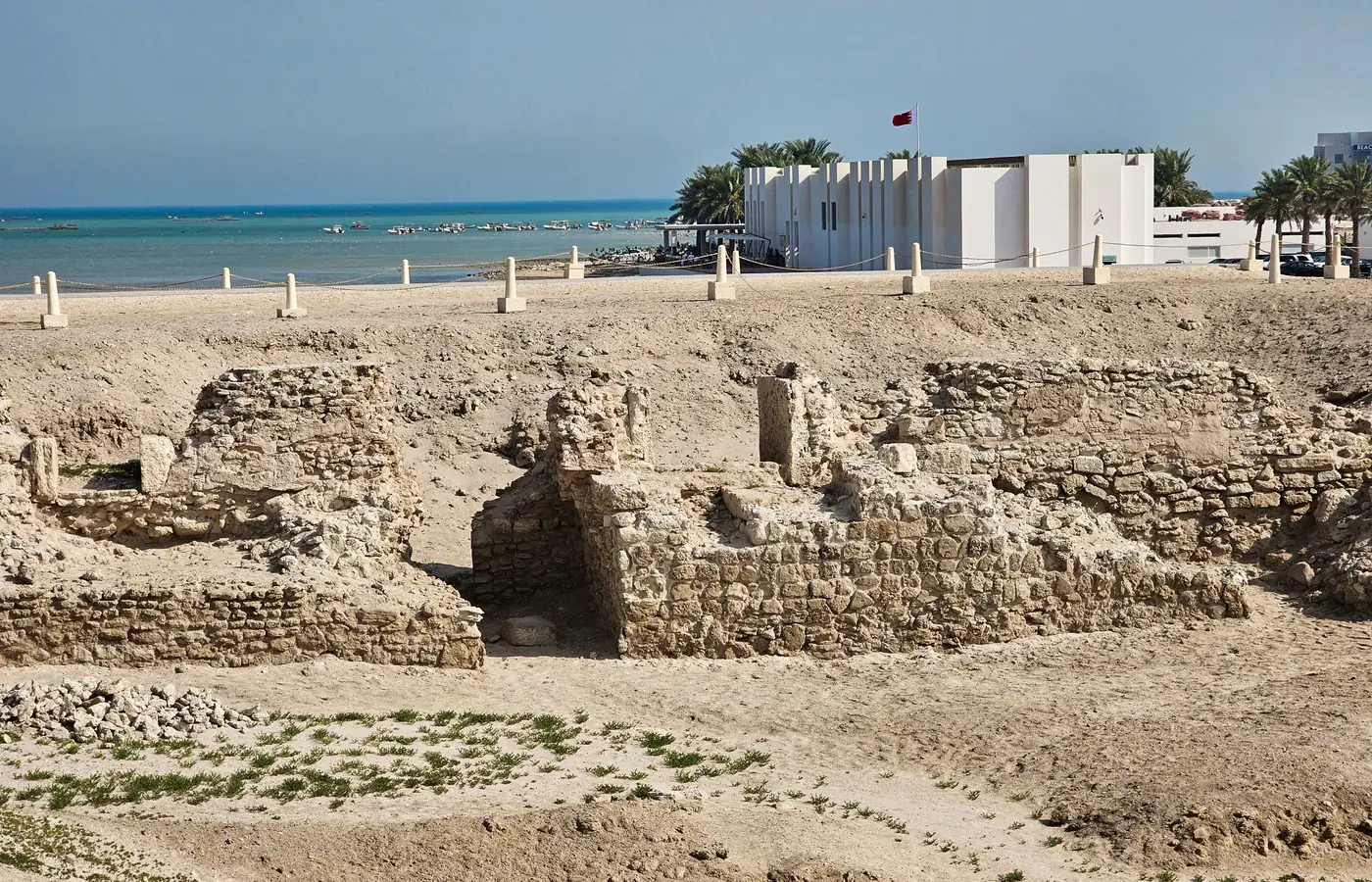 Викопні кам'яні залишки в Qal'at al-Bahrain з музеєм на місці та морем позаду них