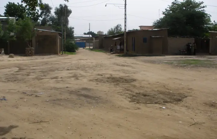 A street in N'Djamena, Chad, lined with low buildings and trees.