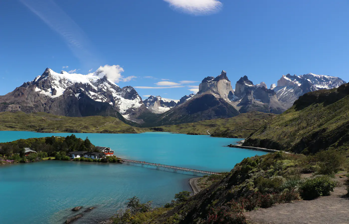 A turquoise lake, a footbridge and jagged mountain peaks in Torres del Paine National Park, Chile.