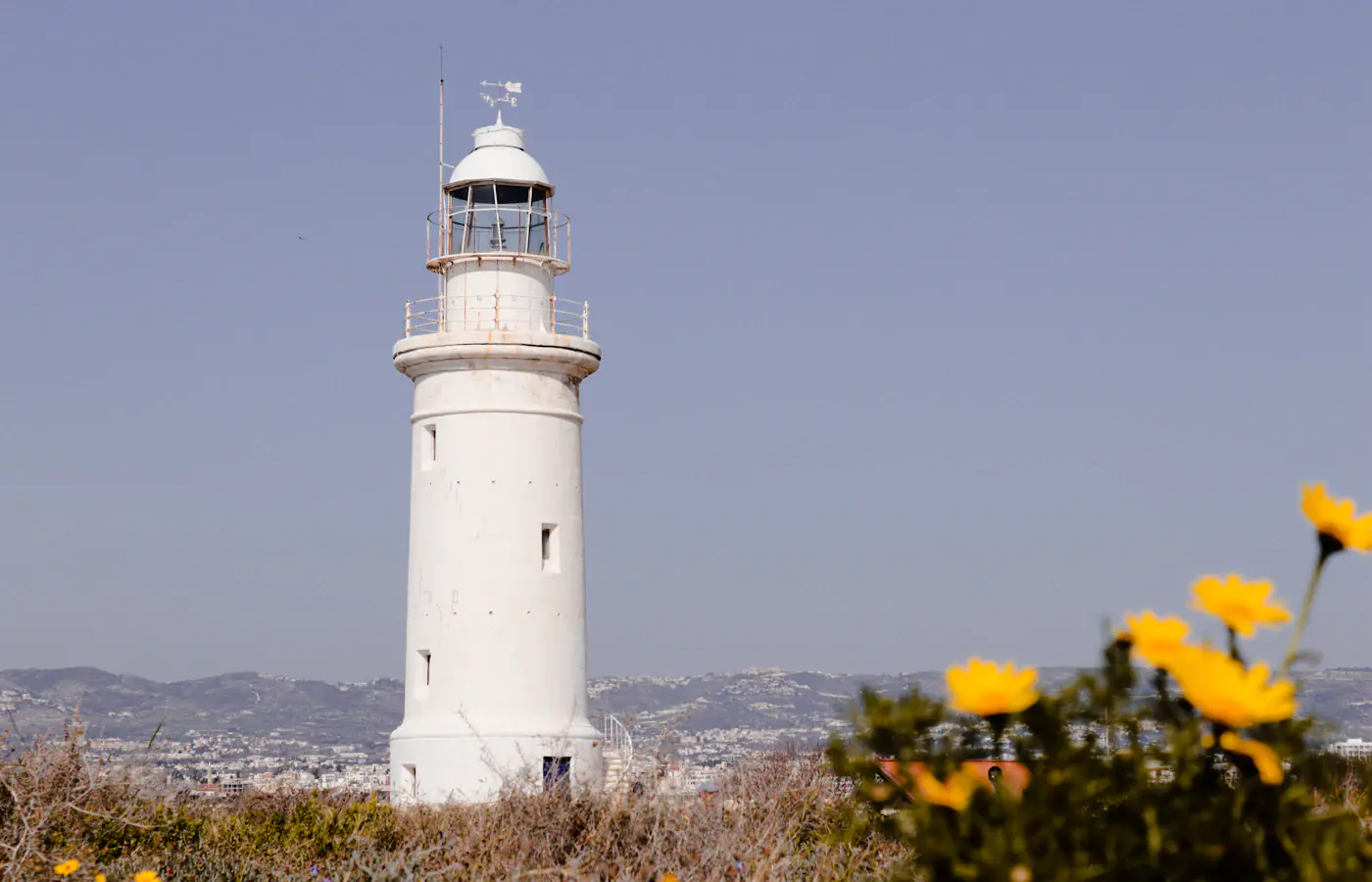 The white Paphos Lighthouse behind yellow flowers in Pafos, Cyprus