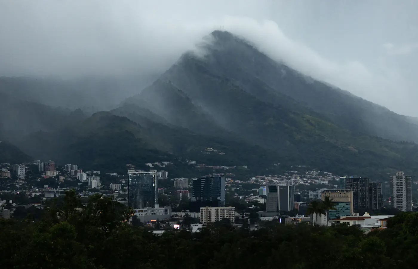 San Salvador high-rises under a cloud-wrapped ridge.
