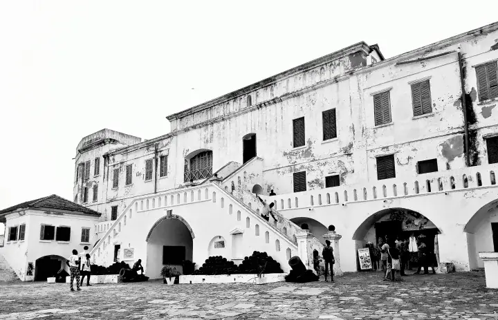 The courtyard, stairs and white walls of Cape Coast Castle in Ghana, shown in black and white.