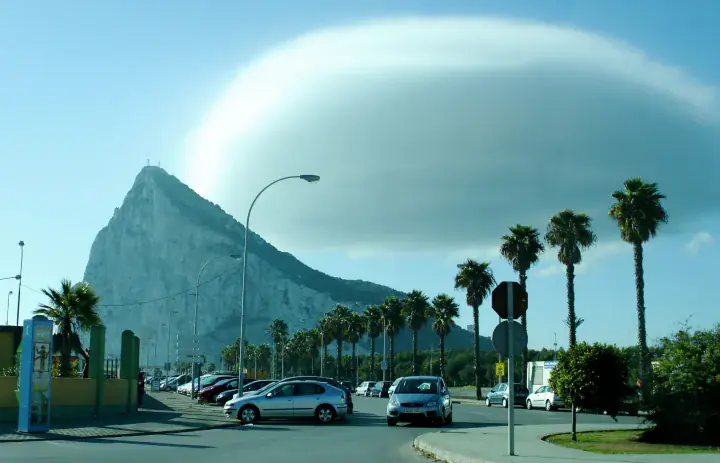 The Rock of Gibraltar viewed from the north, with palm trees and a road in the foreground.