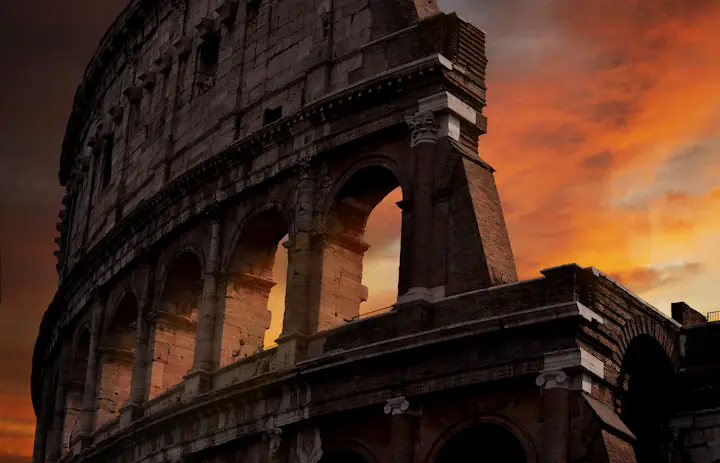 Archi in pietra del Colosseo di Roma sotto un cielo serale arancione.