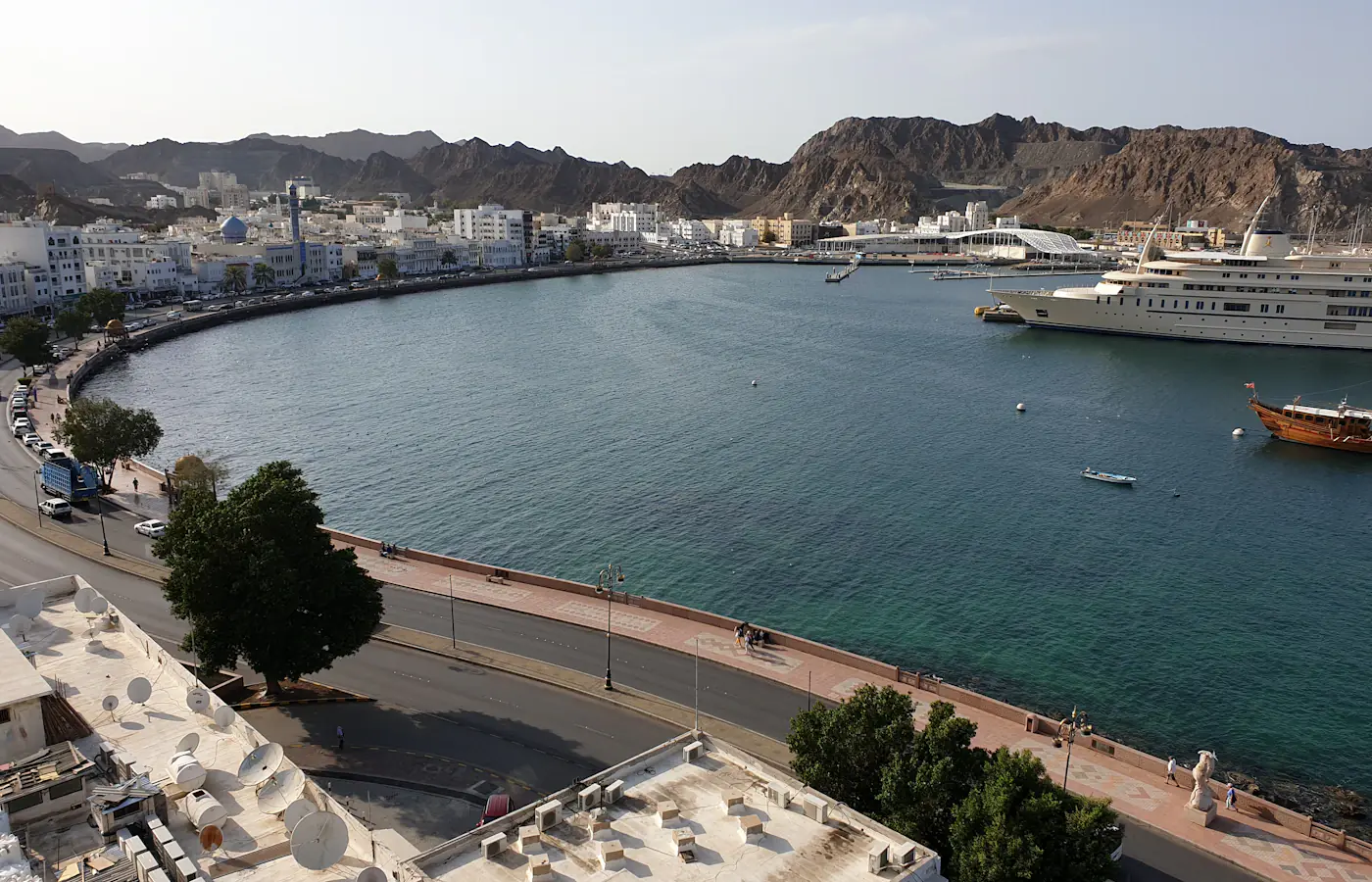 Harbour in Muscat with white waterfront buildings below rocky hills