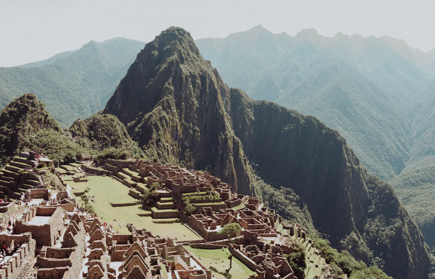 Ancient stone terraces and walls of Machu Picchu with the steep green peak of Huayna Picchu behind, Peru