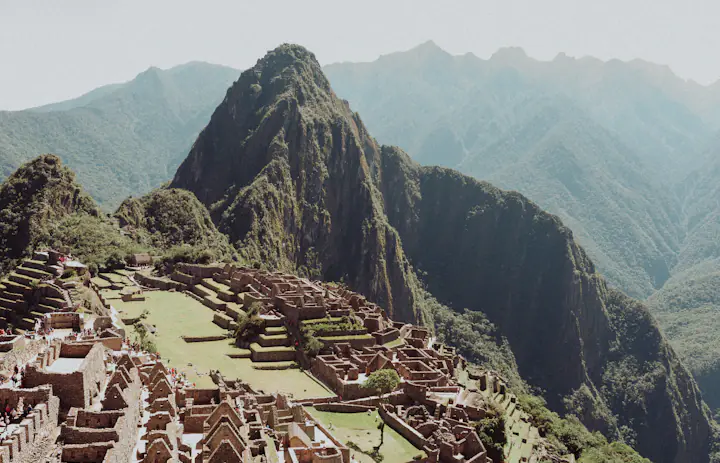 Ancient stone terraces and walls of Machu Picchu with the steep green peak of Huayna Picchu behind, Peru