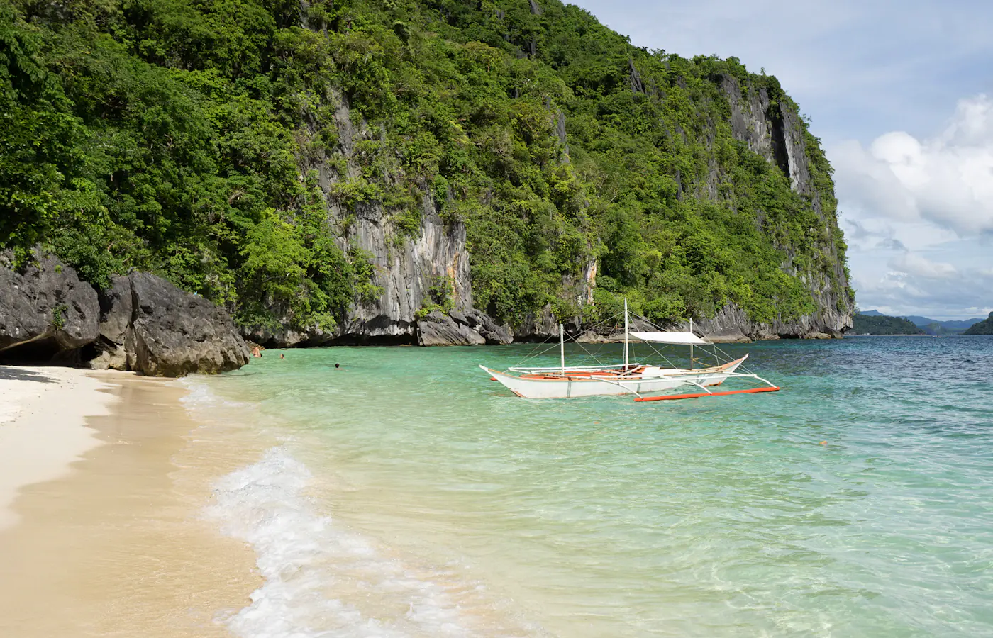 Barca a bilanciere su una spiaggia sotto le scogliere calcaree di El Nido, Palawan