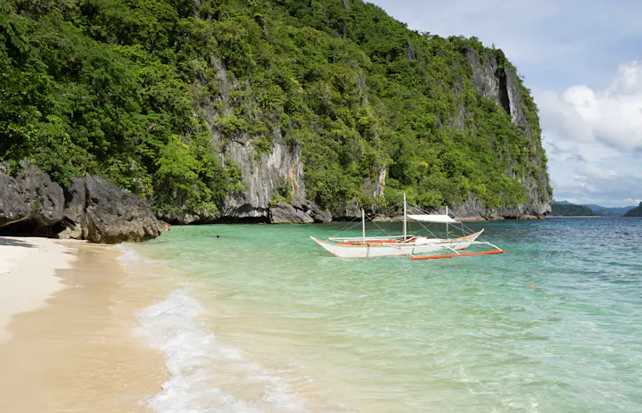 Barca a bilanciere su una spiaggia sotto le scogliere calcaree di El Nido, Palawan
