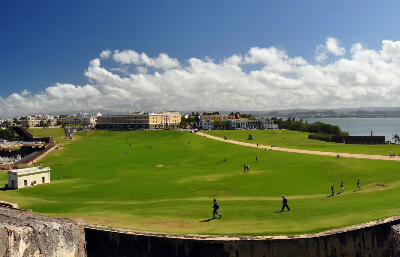 Lawn at El Morro fort with Old San Juan buildings and the Puerto Rico coastline beyond.