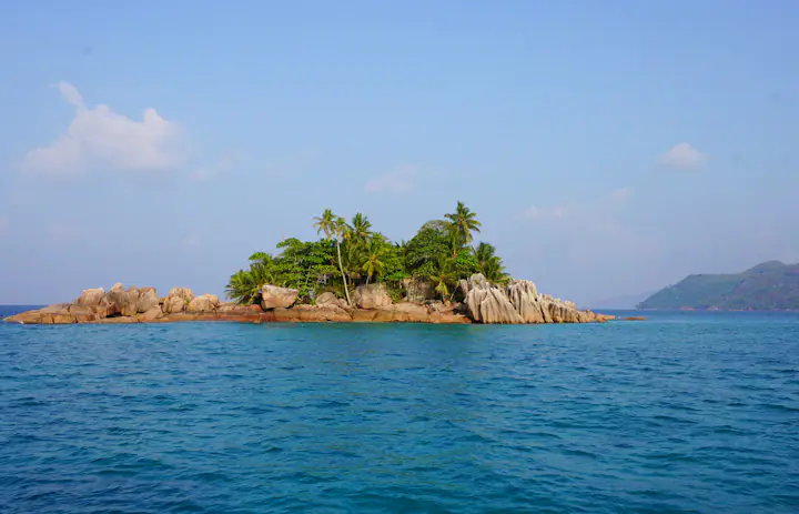 A granite islet with green trees along the coast of La Digue in Seychelles